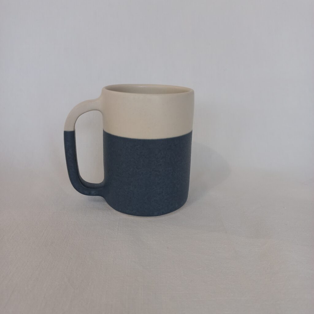 cette image montre une tasse bicolore bleue et blanche en grès avec anse 