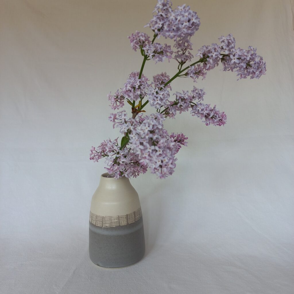 Cette image montre un vase bicolore gris et blanc motif sgraphité en carreaux azvec des fleurs dedans