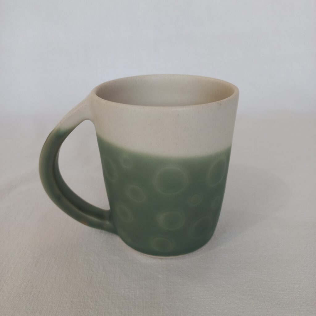 cette image montre une tasse en grès bicolores blanc et vert, le vert est sgraphité en motif rail