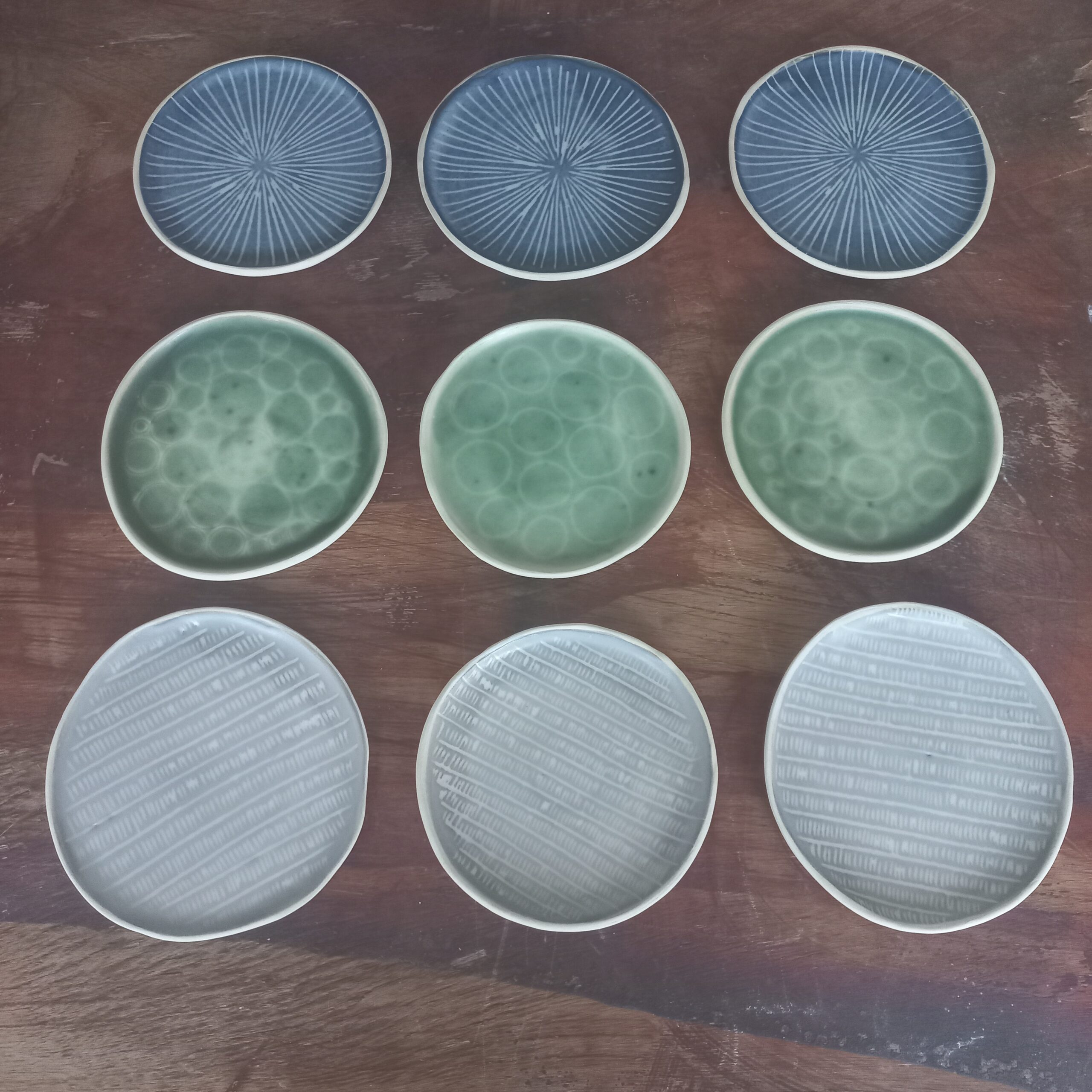 Cette image montre un lot de 9 petites assiettes de 14 cm de diamètre pour vos entrées. elles sont bleues, vertes ou grises et sgraphitiées avec des rayures, des bulles ou un motif rail