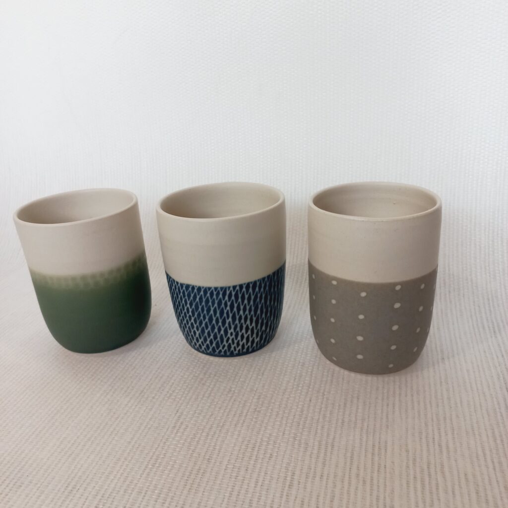 cette image montre un lot de 3 tasses sans anses bicolores blanhe verte bleue et grise etdes motifs à pois sur les parties colorées, forme plus arrondie sur le bas