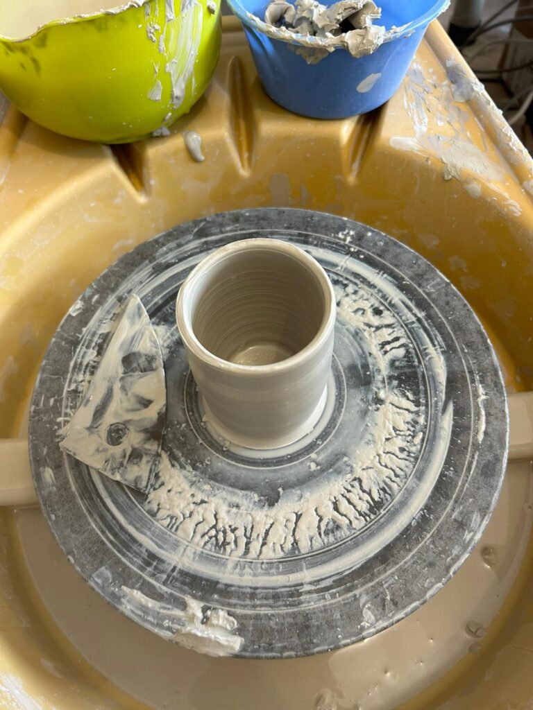 Cette image montre un tour de potier avec une petite tasse en train d'être tournée en grès blanc